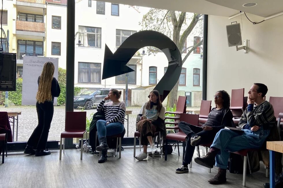 Foto aus dem Workshop zu Klimagerechtigkeit: Teilnehmende sitzen im Halbkreis, Leiterin schreibt etwas ans Flipchart