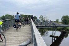 Die Reisegruppe mit dem Rad auf einer Brücke, die in der Mitte einen rechtsknick hat