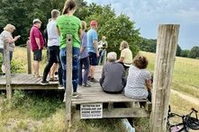 Die Reisegruppe sitzt auf einer Holzplattform auf dem Weyherberg und hört einen Vortrag