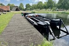 Torfkähne, große dunkle Holzboote ohne Dach, liegen im Wasser an einem Steg