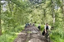 Eine Fahrrad-Reisegruppe fährt über einen schlammigen Weg durch ein Naturschutzgebiet.