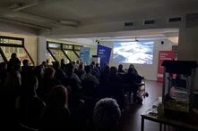 Foto vom Filmabend: Man sieht das Publikum im Halbdunkeln, von hinten fotografiert. An der Seite steht eine Popkornmaschine.