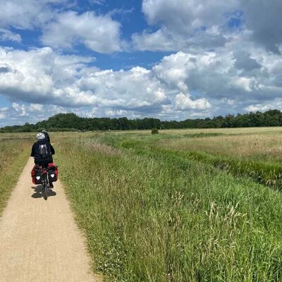 Eine Gruppe von Fahrradfahrenden auf einem Schotterweg durch Überschwmungswiesen