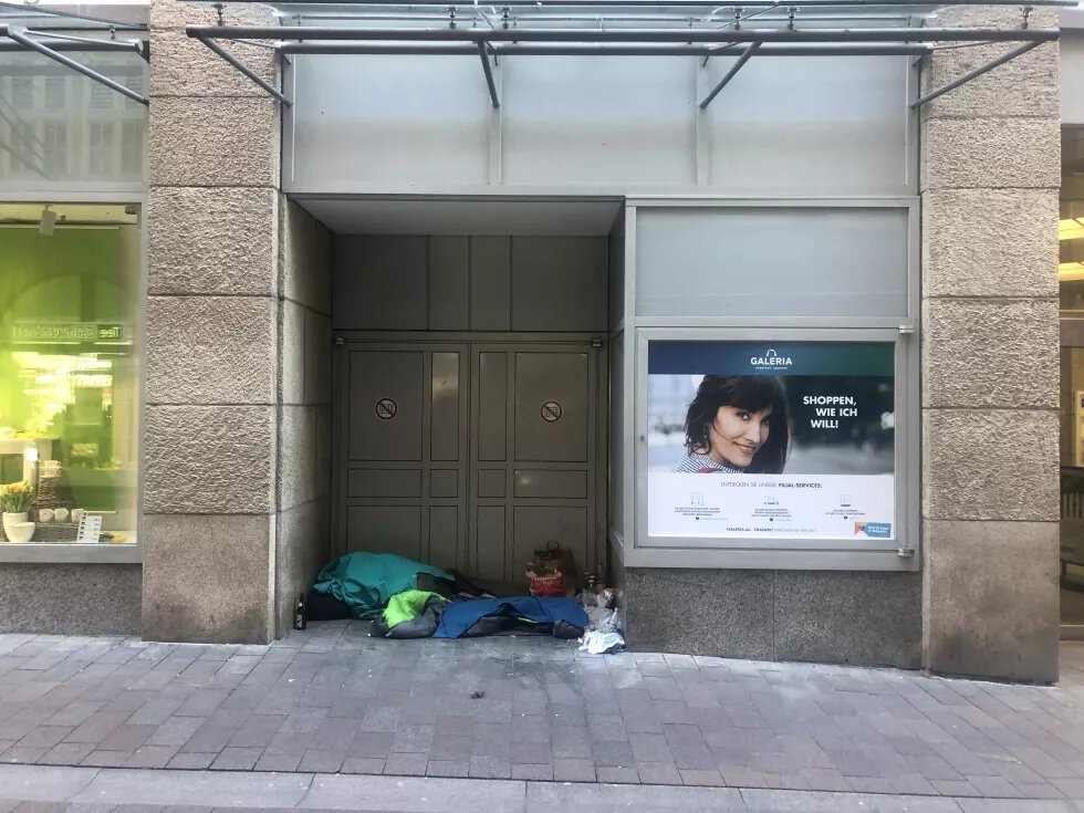 Ein Teaserbild zum Thema Obdachlosigkeit. Es zeigt ein Schlafplatz in einem Unterstand in einer Kaufhausumgebung.