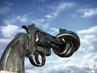 Foto von einer großen Pistole aus Metall, der Pistolenlauf ist verknotet und zeigt in einen blauen Himmel.